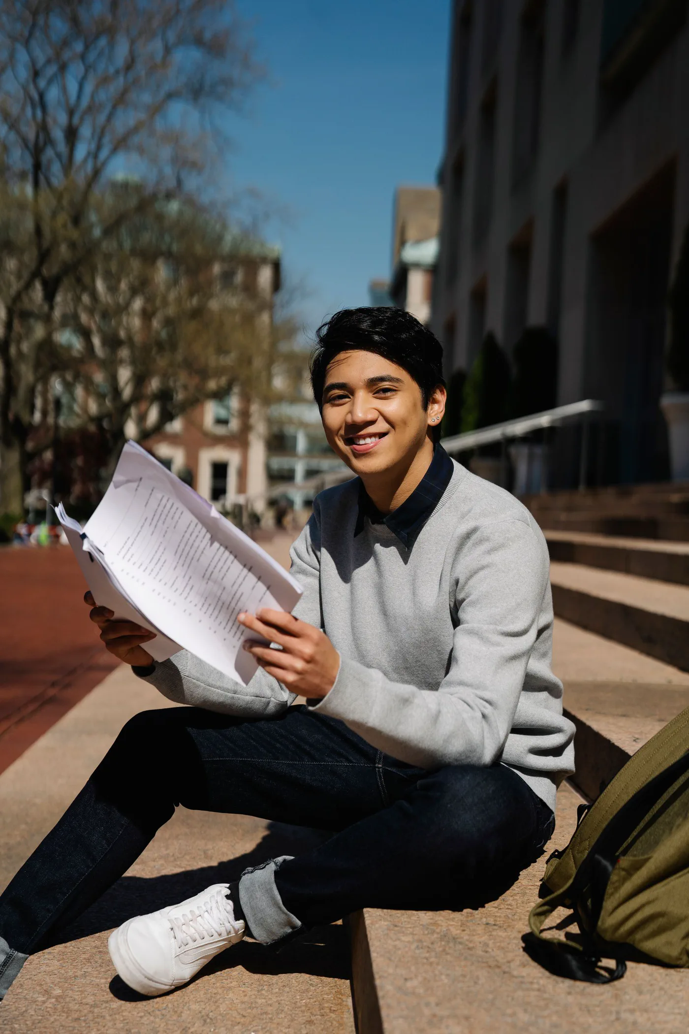 A smiling college student holding study papers on campus